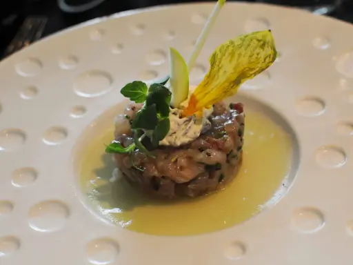 Un tartare de poisson finement préparé, garni de crème, herbes fraîches et d'une fleur jaune, une des spécialités Limoges.