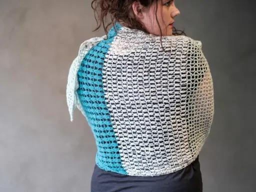 Mujer de espaldas con un cubre hombros a crochet de dos colores, blanco y azul turquesa, con un diseño calado.