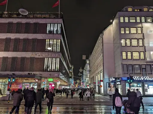 En livlig stockholm shopping street på kvällen. Folk promenerar förbi Åhléns City och Ur & Penn.