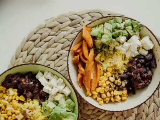 Zwei Schüsseln mit gesunden Reis Rezepten zum Abnehmen: Reis, Bohnen, Mais, Süßkartoffeln, Avocado und Feta.