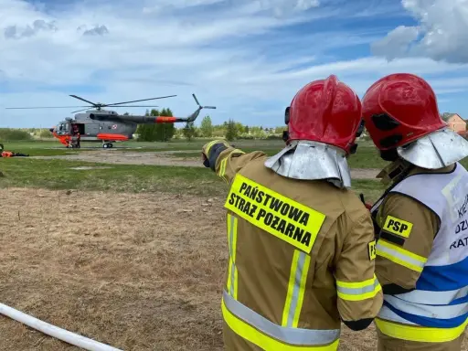 Strażacy w akcji. W tle lądujący śmigłowiec, który wspiera pracę w straży pożarnej.