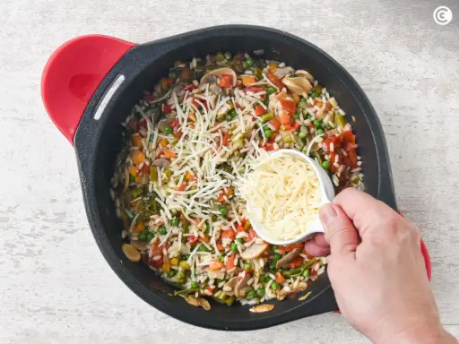 Un delicioso risotto de verduras en una sartén, con queso rallado a punto de ser añadido.