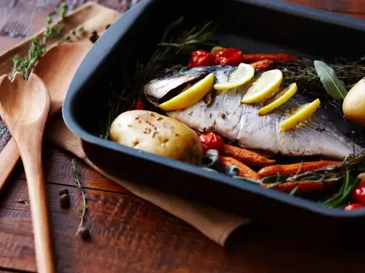 Pescado al horno con patatas, zanahorias y tomates, listo para servir.