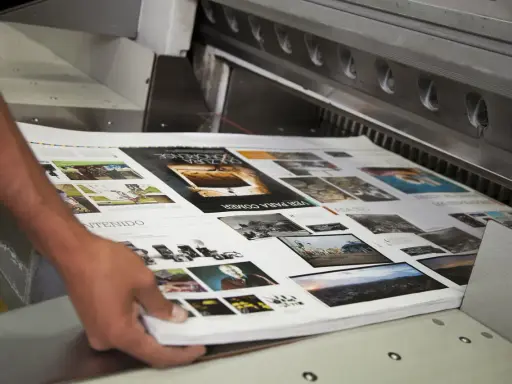 Mani che sistemano fogli stampati su una macchina da taglio, parte della post produzione di una rivista.