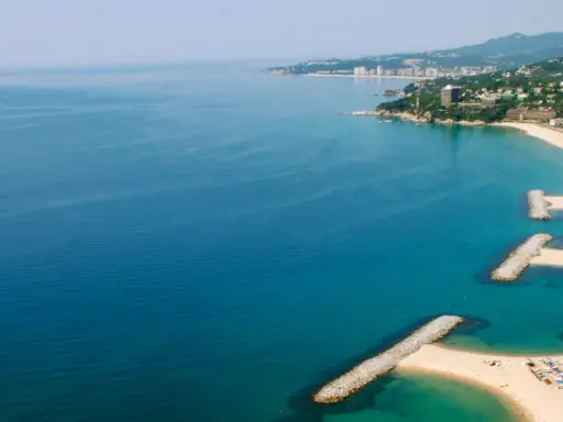 Bucht mit Wellenbrechern und Sandstränden in Calonge, Spanien. Die Küstenstadt erstreckt sich entlang des blauen Meeres.
