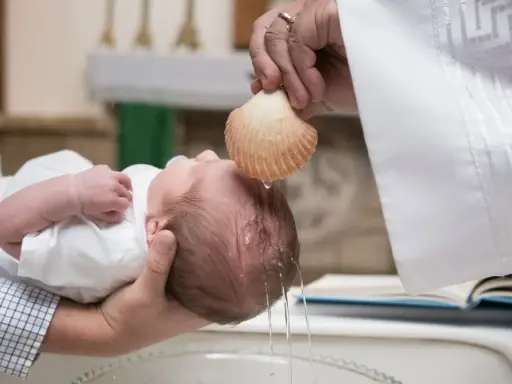 Chrzest dziecka. Kapłan polewa główkę niemowlęcia wodą święconą z muszli. To ważny moment, jak ile daje się na chrzciny.