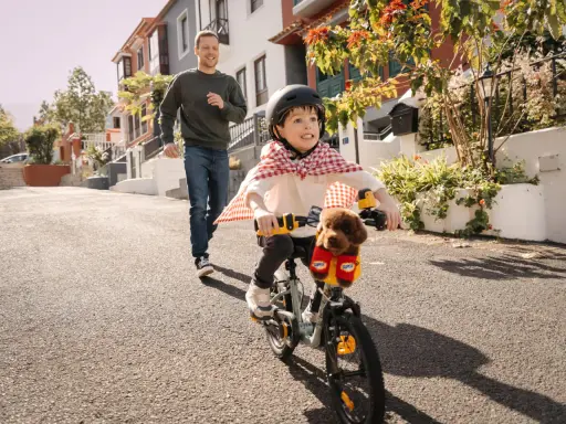 Un bambino con un mantello da supereroe prova ad andare in bicicletta, mentre suo padre corre dietro per aiutarlo. Mio figlio non riesce a pedalare, ma si diverte un mondo!