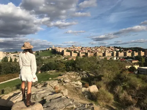 Mujer con sombrero y botas de cowboy admira las murallas de Ávila, un lugar perfecto para visitar con niños.