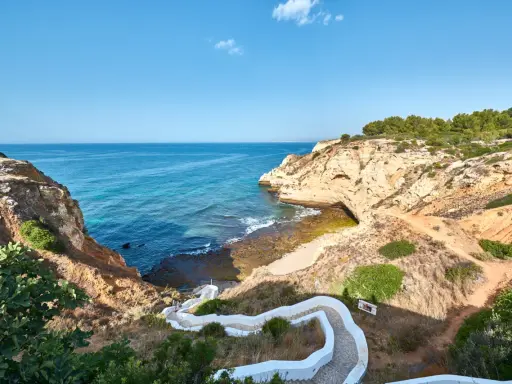 Treppe führt zum malerischen Algarve Meer. Felsformationen und türkisfarbenes Wasser.