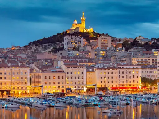 Il porto di Marsiglia MSC, con le luci della città e la basilica di Notre-Dame de la Garde in cima alla collina, crea uno scenario suggestivo al crepuscolo.