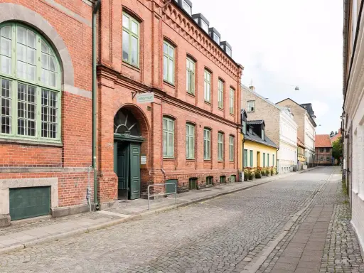 Gammalt tegelhus med gröna fönster och dörrar, en del av ett charmigt vandrarhem i Skåne. Gatsten leder längs en lugn gata.
