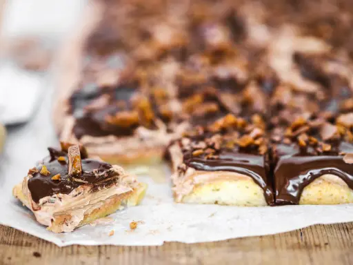 En chokladkaka i långpanna med fluffig chokladkräm och glansig chokladglasyr, toppad med krossad choklad och bitar av godis.