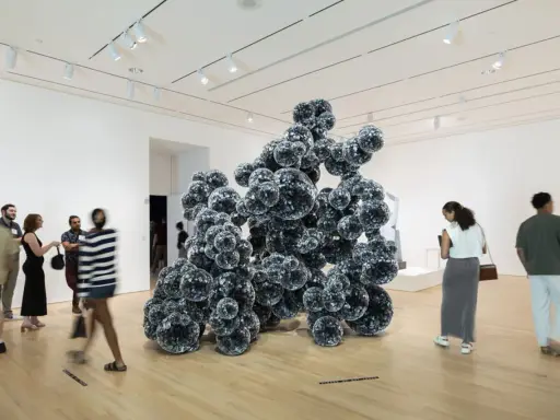 Visitors admire a large, dark, spherical sculpture in a bright gallery space, typical of Indianapolis Museum of Art photos.