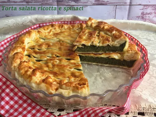Torta salata ricotta e spinaci dorata e invitante, con una fetta tagliata che mostra il ripieno verde e cremoso.