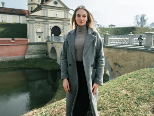 Kobieta w szarym płaszczu i golfie, idealna stylizacja na 14 stopni. W tle zamek i most.