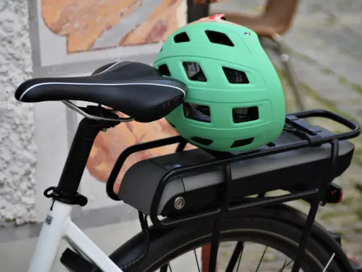 Zielony kask na bagażniku roweru elektrycznego, obok siodełka. Baterie do rowerów elektrycznych są gotowe do długiej podróży.