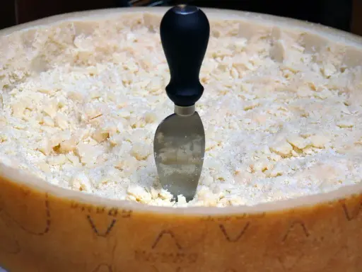 Ein Parmesanrad mit einem Messer, bereit zum Portionieren. Der Unterschied zwischen Parmesan und Pecorino ist oft im Geschmack und der Textur zu finden.