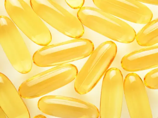 Żółte kapsułki omega 3 ułożone na jasnym tle. Kiedy brać omega 3? Najlepiej po posiłku, by zwiększyć wchłanianie.