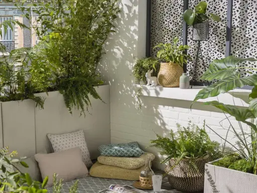 Un coin détente sur un balcon avec une plante brise-vue qui pousse vite en bac, des coussins et des plantes vertes.