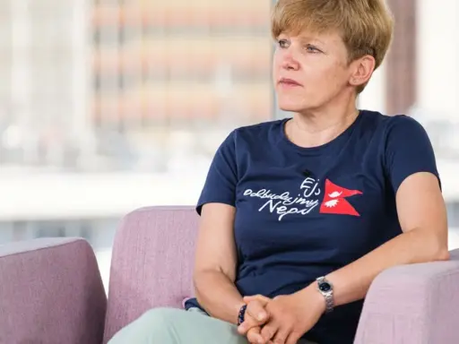 Monika Witkowska w granatowej koszulce z napisem "Odbudujmy Nepal" siedzi w różowym fotelu, patrząc w bok.