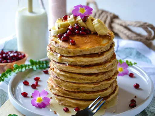 Pile de pancakes healthy garnis de bananes, grenades et fleurs roses. Un délice pour un petit-déjeuner sain.