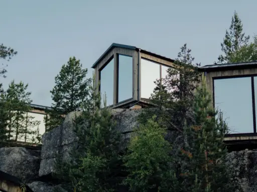 Moderna trähus med stora fönster klättrar uppför en stenig sluttning, omgivna av tallar. En idyllisk camping Lapland resort.