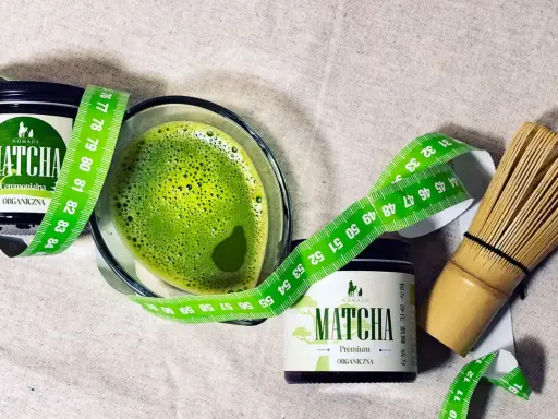 Zielony napój matcha w szklance, obok dwa słoiczki z napisem "MATCHA ORGANICZNA" i miarka krawiecka. Matcha co to? To zdrowy napój.