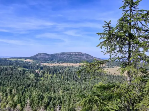 Widok na górzysty krajobraz z lasami i polami, w oddali widać płaskie wzgórze przypominające fort Karola.