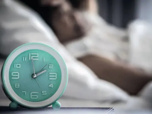 Ein Wecker neben einer schlafenden Person. Die Zeit ist kurz vor 2 Uhr. Ein Symbol für den zirkadianen Rhythmus.