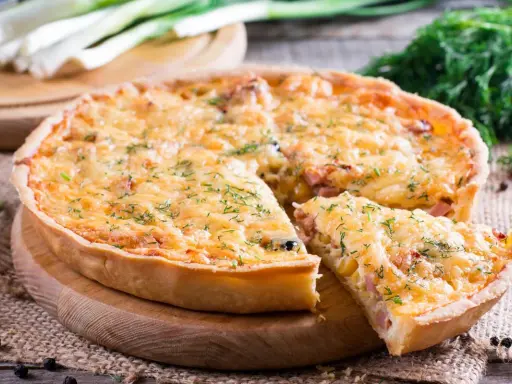 Pyszna tarta z porem i boczkiem, posypana serem i koperkiem, z kawałkiem już wyjętym.