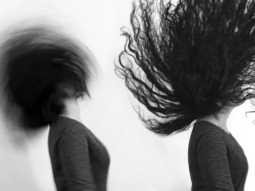 Dos cabezas con cabello largo y oscuro en movimiento, capturadas con un obturador fotográfico que crea un efecto de desenfoque dinámico.