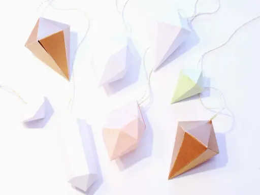 Papierdiamanten in verschiedenen Farben und Größen, die an goldenen Fäden hängen. Eine tolle Idee für eine diamant basteln vorlage.