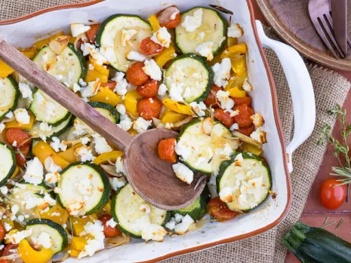Gebackener Feta mit Zucchini, Kirschtomaten und gelber Paprika in einer Auflaufform, bereit zum Servieren.