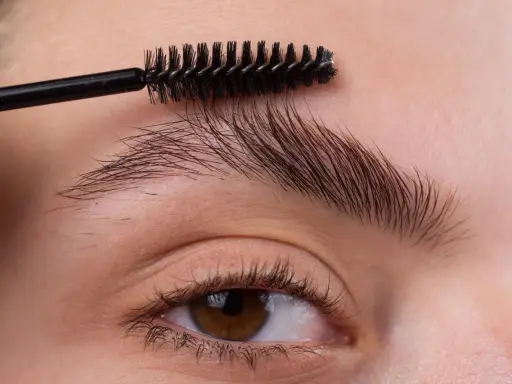 Une brosse à cils peigne les sourcils d'une femme pour les mettre en forme.