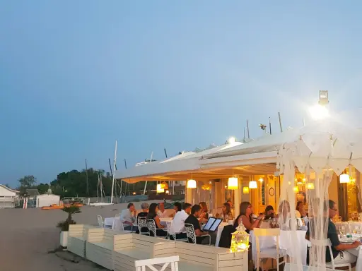 Serata in uno dei ristoranti della Riviera Romagnola, con tavoli apparecchiati sulla sabbia e luci soffuse.