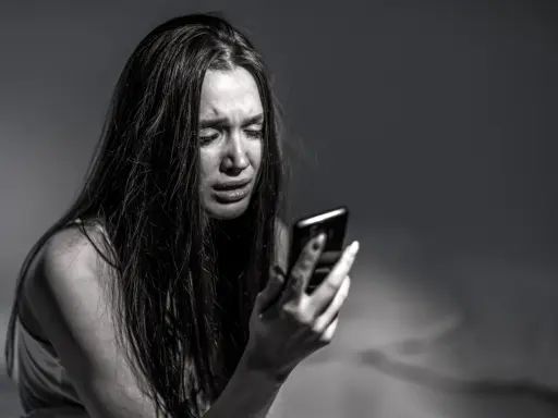 Ragazza piange guardando il telefono, vittima di revenge porn. La legge punisce chi diffonde immagini private senza consenso.