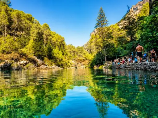 Un refrescante charco del aceite, rodeado de vegetación exuberante y rocas, con gente disfrutando del día.