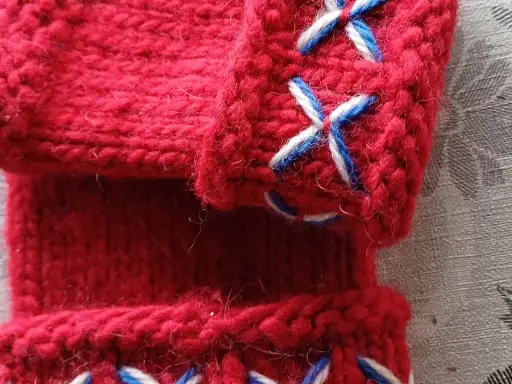 Närbild på röda, stickade vantar utan fingrar med korsstygn i vitt och blått. Perfekt för att virka vantar utan fingrar.