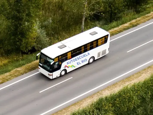 Autobús blanco de la autoescuela El Río en una carretera, preparándose para un examen en la pista.