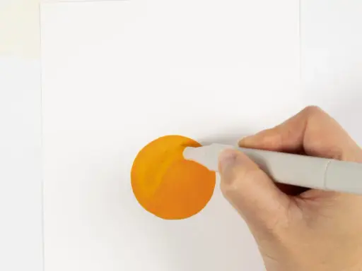 En hand håller en grå tuschpenna och målar en orange cirkel på vitt papper.