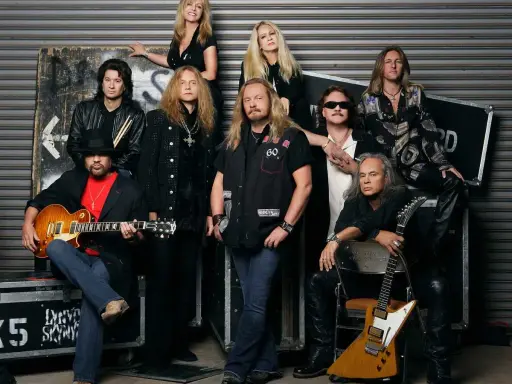 Medlemmar av Lynyrd Skynyrd poserar för ett gruppfoto. En man i förgrunden håller en gitarr.