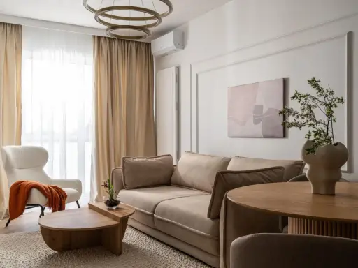 Nowoczesny salon szaro beżowy z wygodną kanapą, puszystym fotelem i drewnianymi meblami.