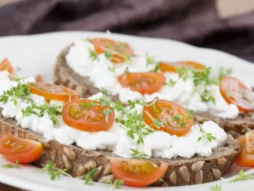 Kanapki z ciemnego pieczywa z twarożkiem, pomidorkami koktajlowymi i kiełkami.