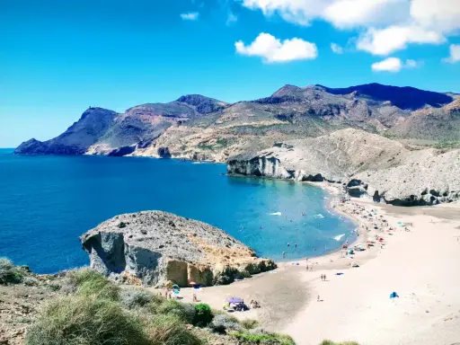 Sonnige playa de mónsul mit türkisfarbenem Wasser, Bergen und vielen Badegästen.