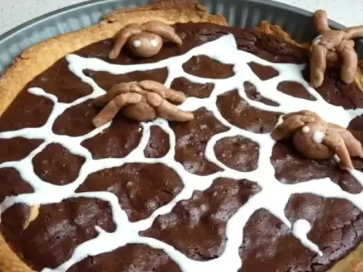 Tarte au chocolat d'Halloween décorée d'une toile d'araignée en glaçage blanc et d'araignées en pâte d'amande.