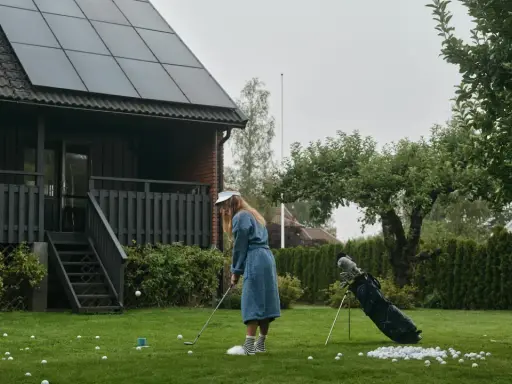 En flicka övar golf framför ett hus med solceller på taket. Solceller ger ren energi.