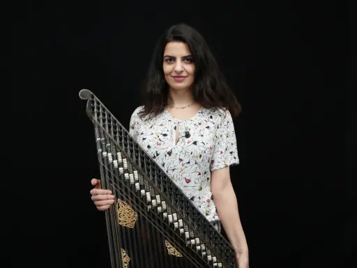 Une musicienne tient un kanoun, instrument de musique à cordes pincées, devant un fond noir.