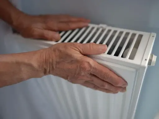 Manos sobre un radiador blanco, sintiendo el calor. El radiador hace ruido, quizás por el agua circulando.