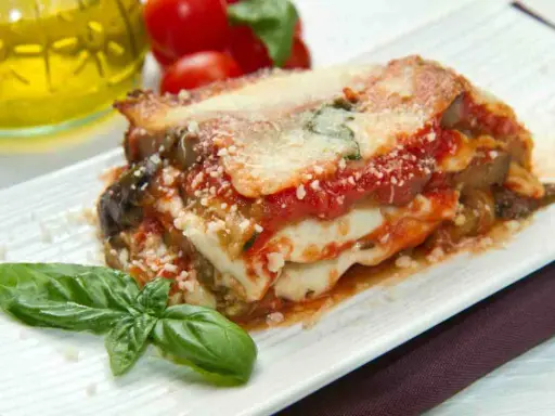 Una fetta di parmigiana di mare pugliese, con melanzane, pomodoro e mozzarella filante, guarnita con basilico fresco.