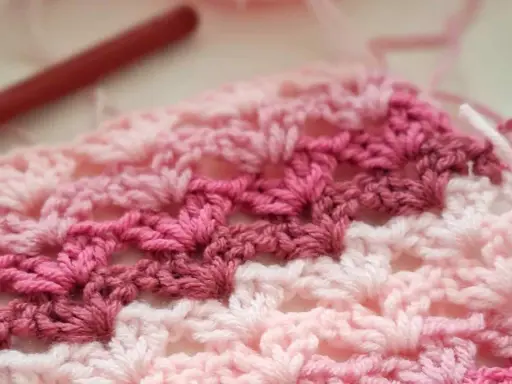 Tejido a crochet con hilo rosa y blanco. Un patrón de chaleco fácil en progreso, con un ganchillo rojo al fondo.